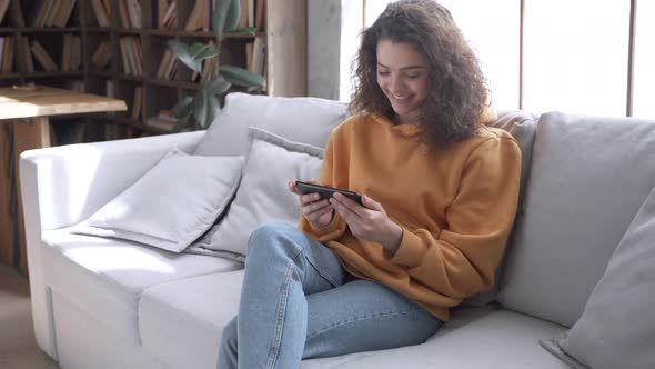 Happy Hispanic Girl Sit on Sofa Hold Phone Video Calling Online in Mobile App