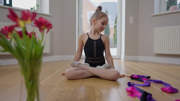 Front View Wide Shot of Slim Charming Teen Gymnast Sitting in Lotus Pose with Ribbon on Floor