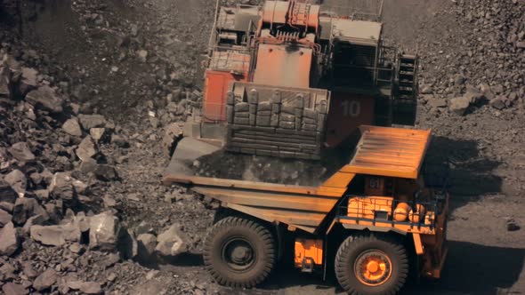 Close-up yellow excavator shovels ore with a bucket in a quarry.