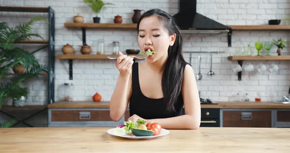 Asian Woman Sitting at Table Looking Sad and Bored with Diet Not Wanting to Eat Salad