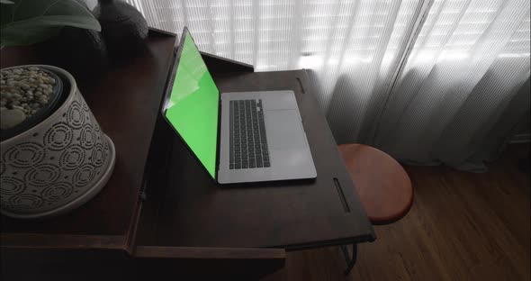 Laptop computer with green screen on modern wooden desk. Steadicam slowly rotates around.