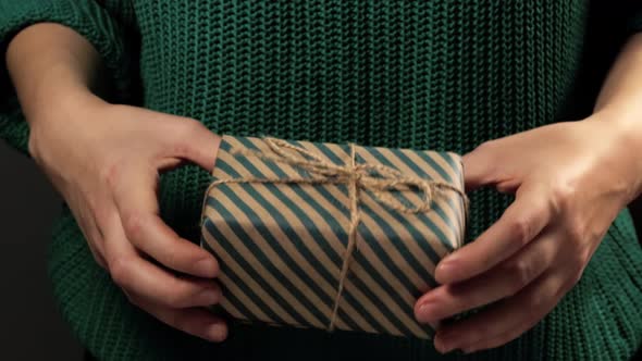 Girl  hand holding a gift wrapped in striped green-brown paper tied with a rope