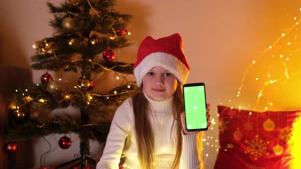 Cute Little Girl in Christmas Hat Holding Mobile Phone with Green Screen