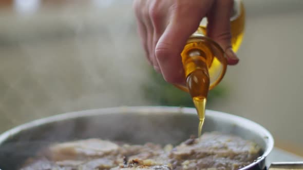 Woman pouring oil to pan with veal shank