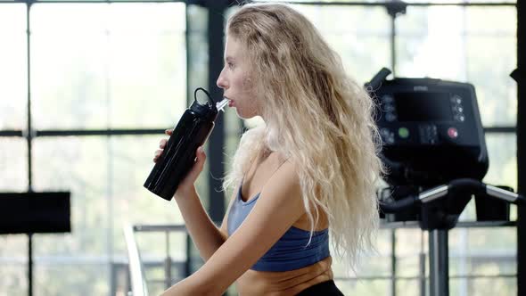 Athletic Woman Drinks Water From a Bottle and Rests After Training in the Gym