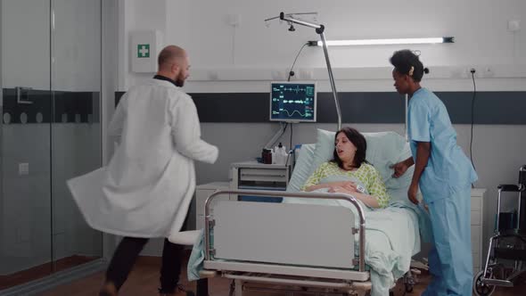 Black Assistant Helping Patient to Sit Comfortable in Hospital Ward