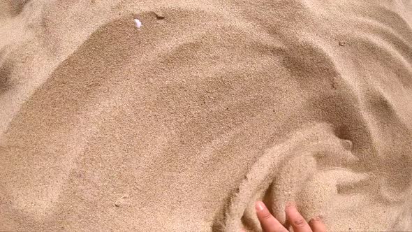 Person Runs His Hand Over Surface of Sand and Scatters It with His Fingers