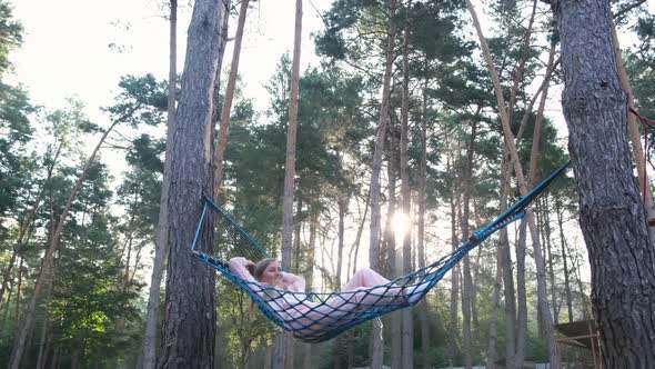 Young cute girl resting lying in a hammock in the woods.