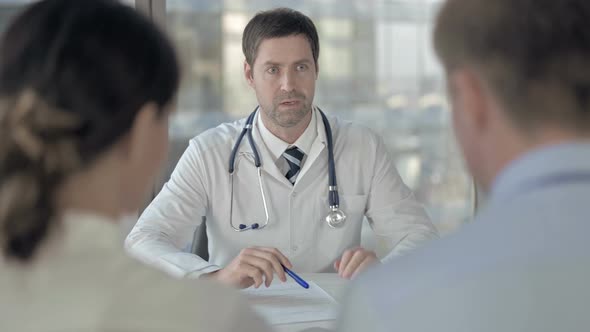 Rear Back View of Couple Having Conversation with Middle Aged Doctor