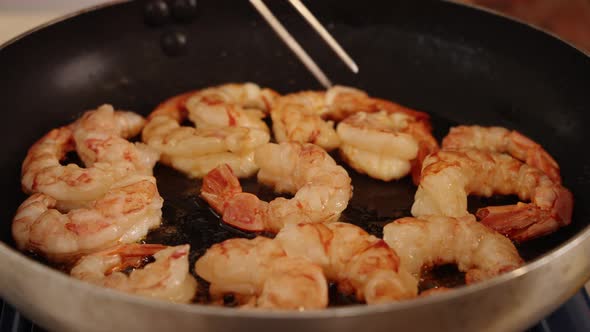 Delicious shrimps browning on hot oil pan, chef using tongs to grab and flipping sides and sauteing