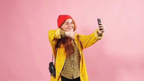 Red-haired Girl Tourist in a Yellow Cloak Communicates with Friends on Skype.