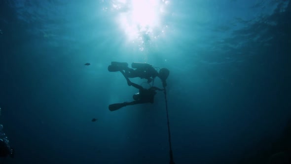 A silhouette of two scuba divers underwater holding onto a buoy swaying in the current