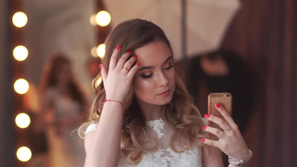 Beautiful Girl Model Posing in Front of a Mirror and Taking Pictures on a Smartphone.