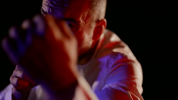 a Man in an Unbuttoned White Shirt Strikes with His Hands on a Dark Background