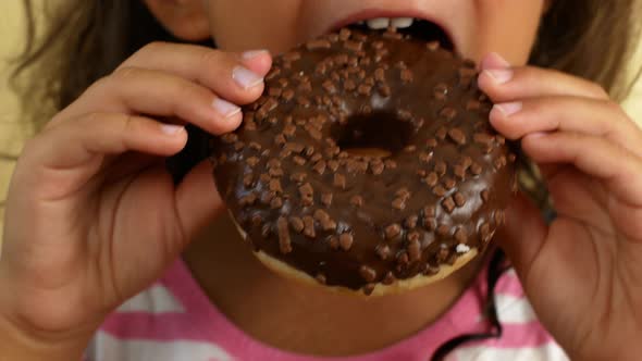 The child is holding a sweet tasty donut in his hands. Child chews and licks his lips from eating