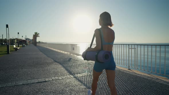 Sporty Young Athletic Girl with a Yoga Mat Walking Over a Bridge