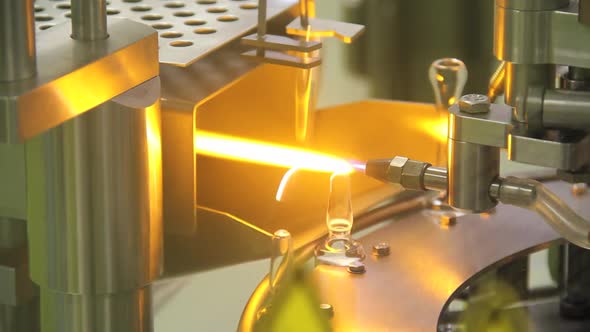 Filled glass medical vials being sealed by fire in machine.