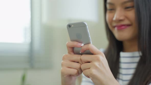 Asian beautiful woman sit on sofa and chat on mobile phone in house.