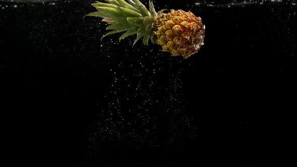 Tropical Fruit Pineapple Rotating and Falling Into Water with Splash Bubbles on Black Background