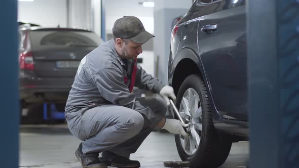 Side View of Adult Professional Tightening Screws on Car Wheel. Caucasian Male Auto Mechanic Working