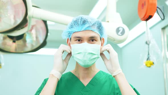 Portrait of Asian surgeon with medical mask standing in operation theater at a hospital. Team of Pro