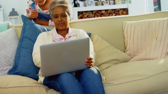 Grandmother and granddaughter using laptop in living room