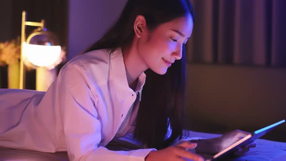 Young Asian beautiful woman enjoy using smartphone- tablet   in bedroom at night time.