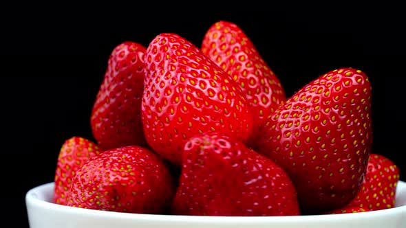 Strawberries without tails lie in white bowl or plate. It rotates