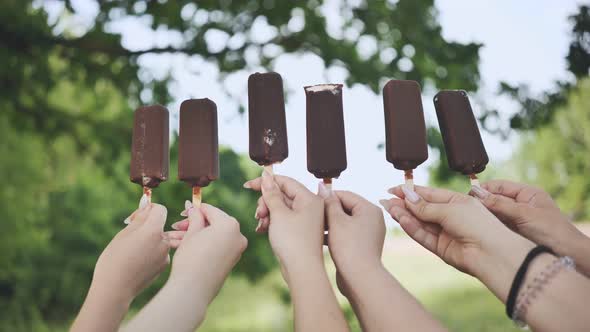 Friends Hold Chocolate Ice Cream on a Stick in a Row