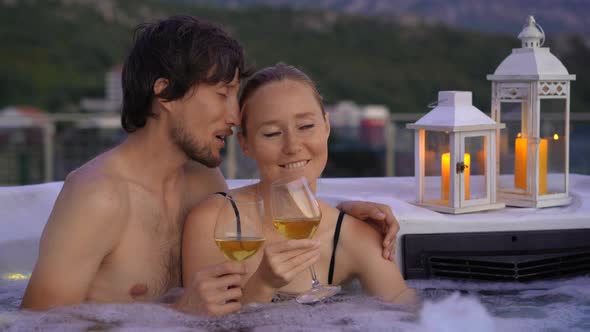 A Young Man and Woman are Relaxing in the Hot Tub on a Rooftop with a View on Mountains During