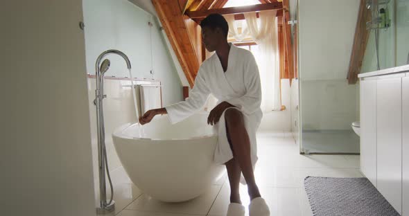 African american attractive woman in white robe sitting on bathtub, preparing bath