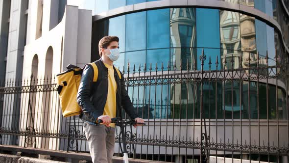 Delivery Man with Yellow Bagpack and Protective Mask Riding Electric Scooter Through the City with