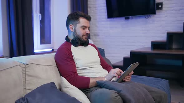 30-Aged Guy Sitting on the Couch and Browsing Apps on I-pad