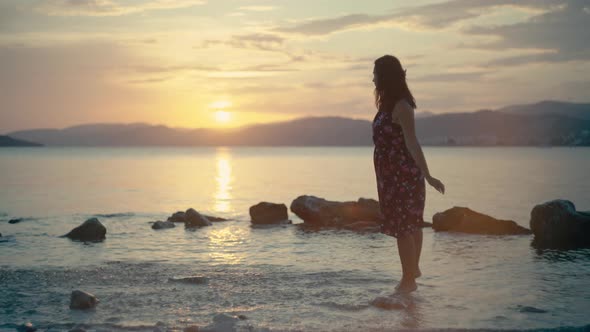 Girl Splashes Water with Her Feet in the Sea at Sunset