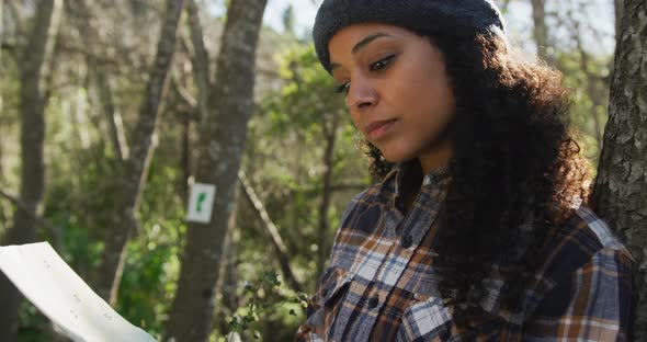 Biracial woman checking map in forest during hiking in countryside