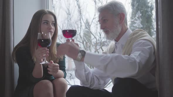 Confident Senior Caucasian Man Talking About Wine with Young Pretty Woman. Grey-haired Male Retiree