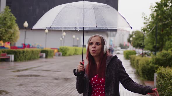 Young Beautiful Woman with Transparent Umbrella Dancing in Rain on City Street