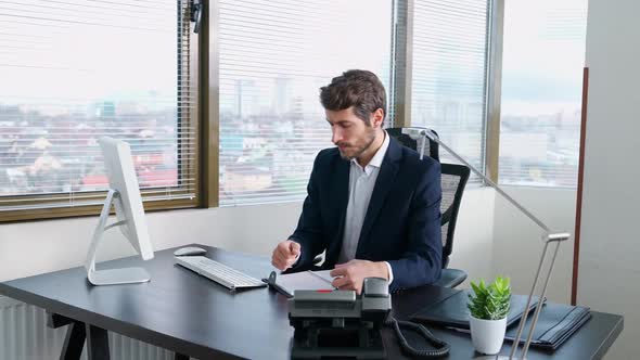 Businessman Working at a PC Sitting at Work Desk Manager Writes the Information in a Notebook Works