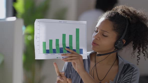 Video Chat POV of Confident Beautiful Slim Woman in Earphones Talking Pointing at Business Graph