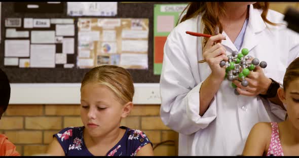 Teacher assisting school kids with molecule model in laboratory