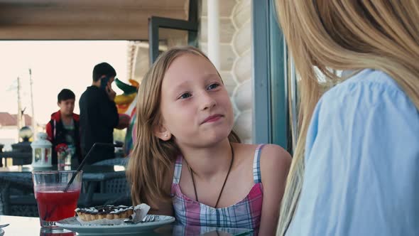 A Beautiful Blonde Girl is Talking to Her Mom in a Cafe