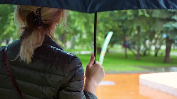 Elegant Woman in Glasses Stands with an Umbrella in the Park