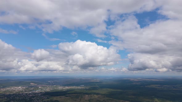 Aerial View From High Altitude of Distant City Covered with Puffy Cumulus Clouds Flying By Before