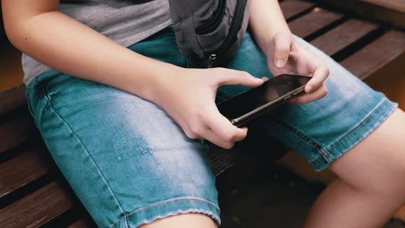 Child Playing Video Games on a Smartphone in Park Outdoors Sitting on a Bench