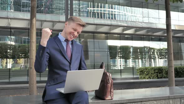Businessman Celebrating Results on Laptop Sitting Outside Office