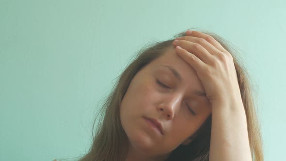 Stressed brown hair woman with headache on mint background Tired lady without make-up feel pain