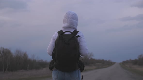 Healthy Woman Traveler with a Backpack in a Protective Medical Mask and a Hood Is Walking Out of