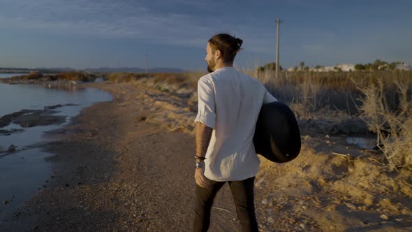 Ack View of Male with a Guitar Walking on Sandy River Coast at Sunset Alicante Spain