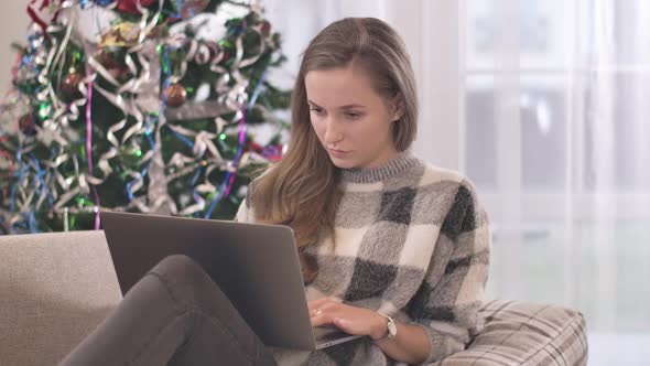 Portrait of Concentrated Young Woman Using Laptop on Christmas Weekends. Beautiful Brunette