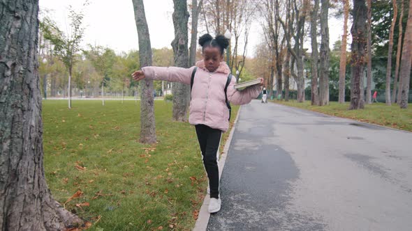 African American Little Girl Walking on Curb Border Balancing Way From School in Urban Park Afro
